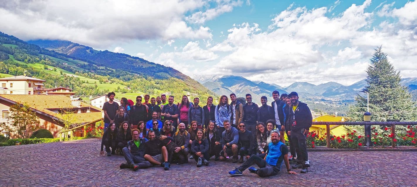 Un viaggio di gruppo WeRoad posa per una foto su una terrazza di ciottoli con montagne verdi e un villaggio sullo sfondo.