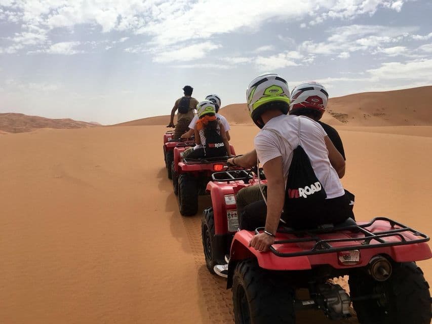 Un voyage de groupe WeRoad à dos de quads rouges en file indienne à travers les dunes de sable du désert sous un ciel nuageux.