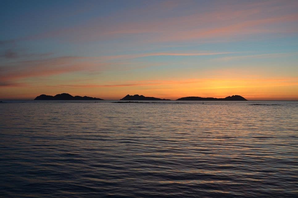 Islas distantes se siluetean contra un cielo de atardecer colorido sobre el mar en calma y ondulante.