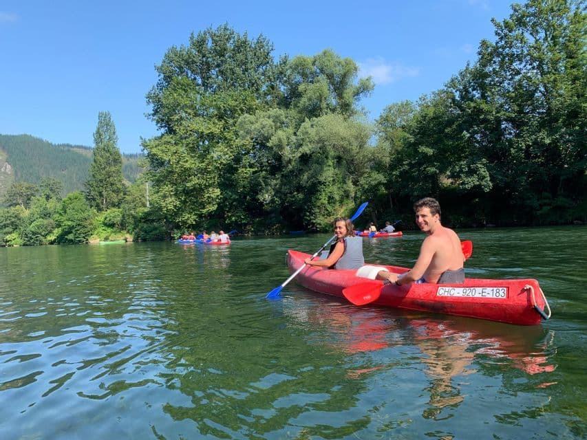 Un hombre y una mujer de un viaje en grupo de WeRoad sonríen mientras reman en una canoa roja en un río, con otras canoas de fondo.