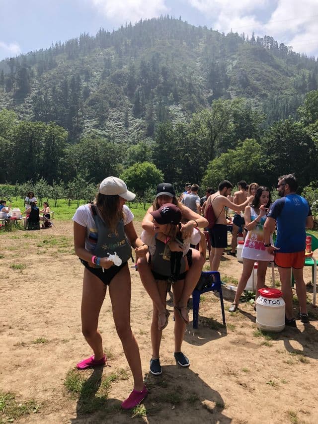 Un viaje en grupo de WeRoad divirtiéndose al aire libre, con una mujer llevando a otra a cuestas frente a una montaña verde y boscosa.