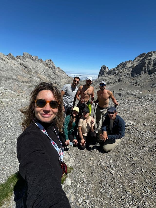 Un grupo de WeRoad se toma una selfie mientras hace senderismo en un valle de montaña rocoso bajo un cielo azul claro.