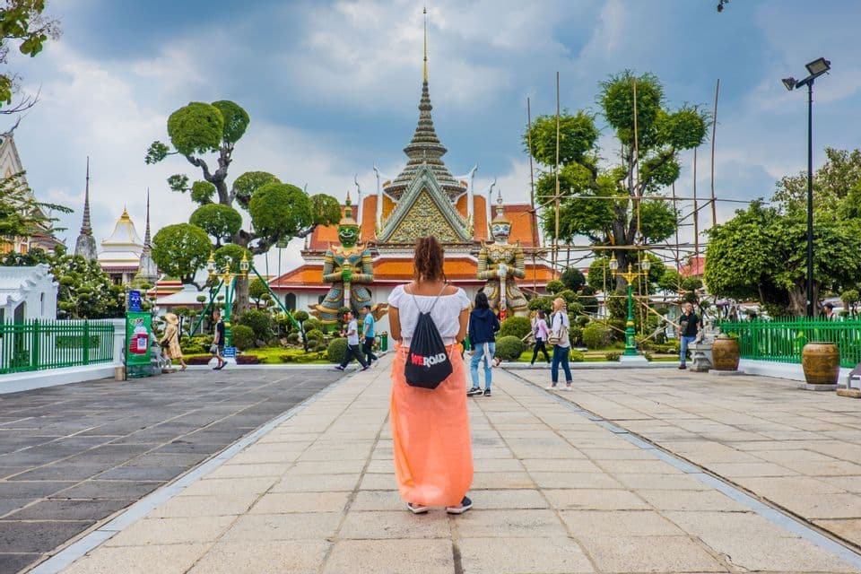 Una mujer de espaldas con una mochila WeRoad mira un templo grande y ornamentado flanqueado por dos estatuas gigantes en un patio.