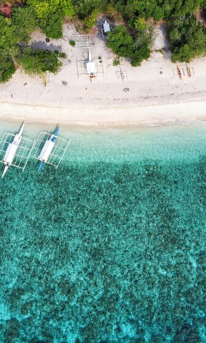Una vista aérea cenital de barcos con estabilizadores amarrados junto a una playa de arena blanca con agua turquesa cristalina y árboles verdes.