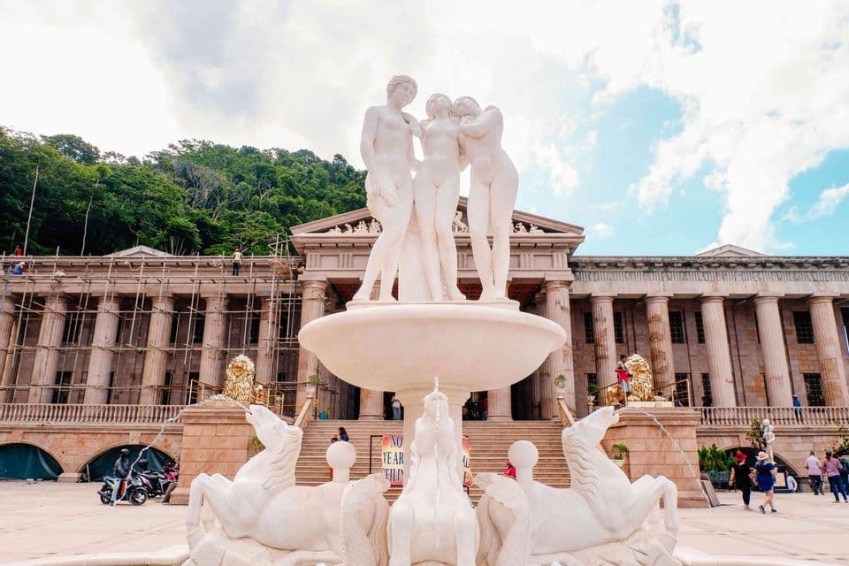 Una gran fuente de mármol blanco con estatuas de tres mujeres se alza frente a un edificio clásico con andamios.