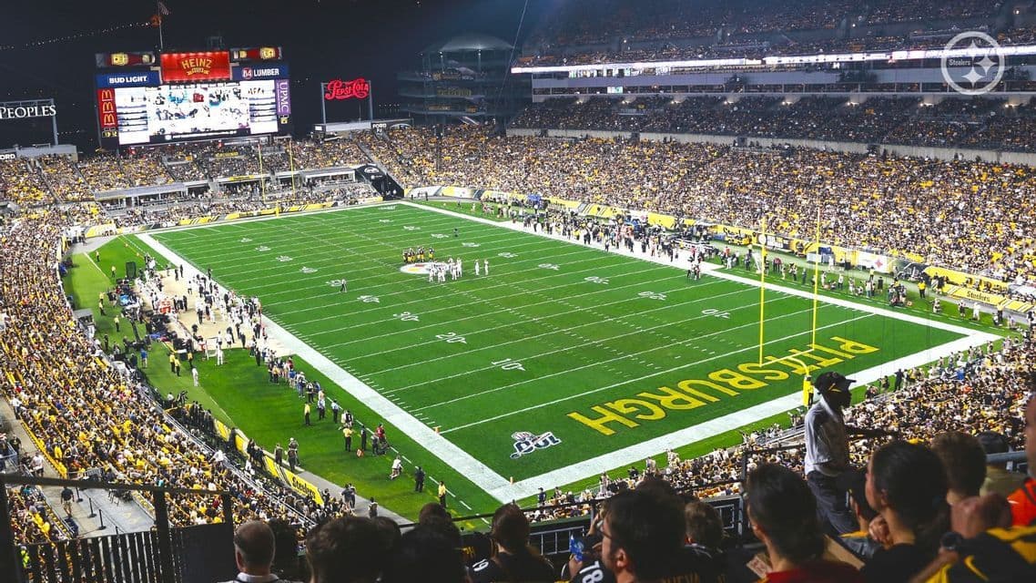 Una veduta aerea di uno stadio di football americano gremito di notte, con i giocatori in campo e 'Pittsburgh' visibile nell'end zone.