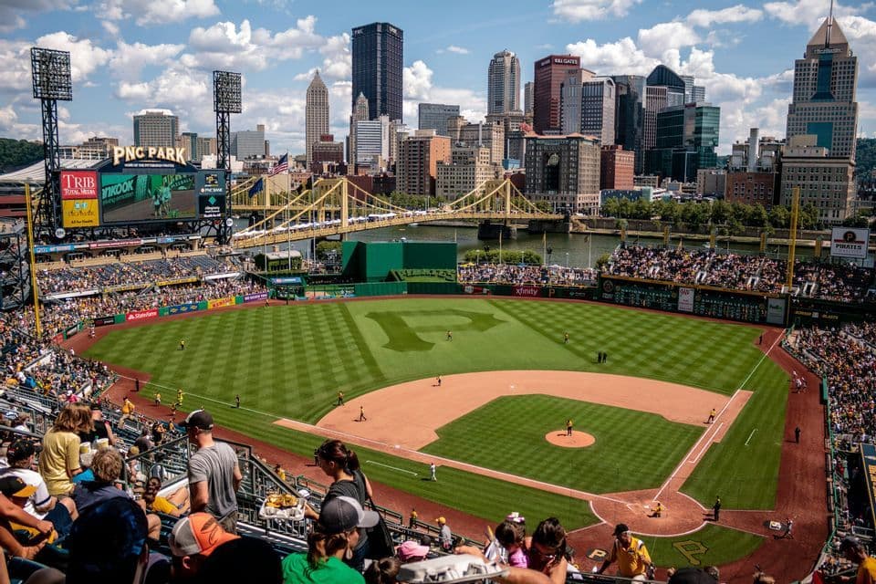 Una vista dall'alto di una partita di baseball al PNC Park, con lo skyline della città e un ponte giallo sullo sfondo.
