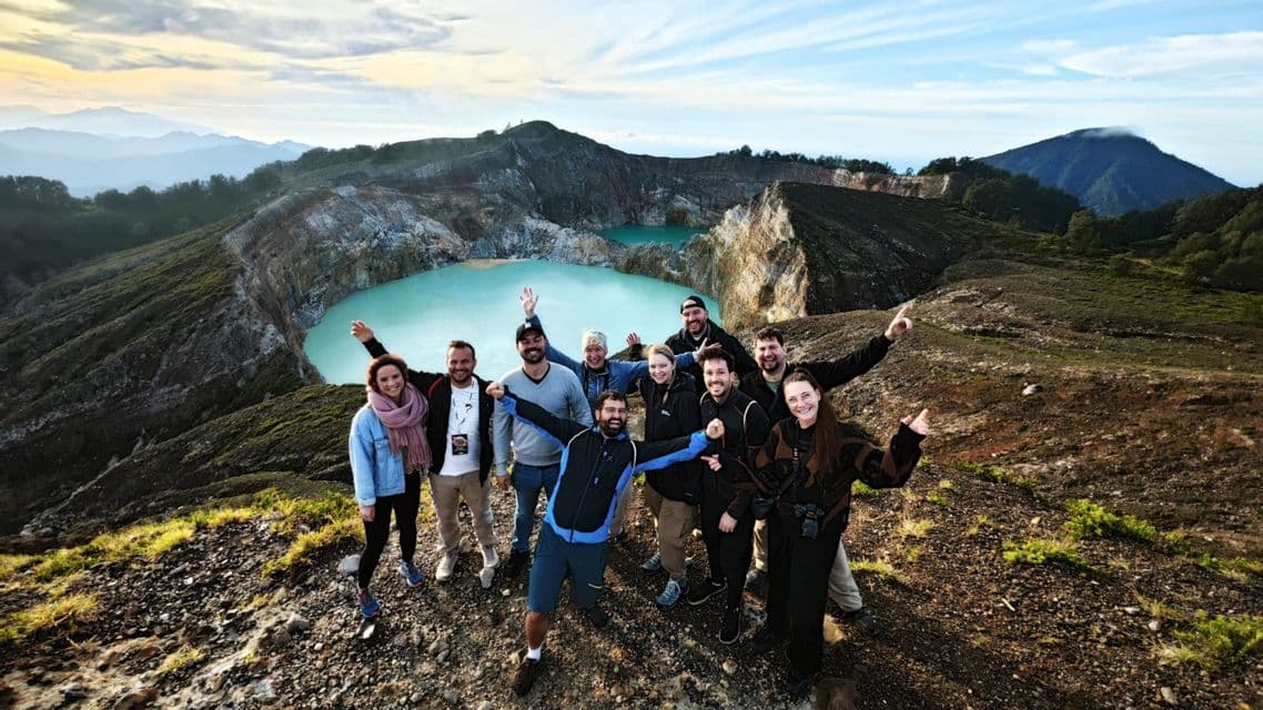 Eine WeRoad-Gruppenreise posiert für ein Foto auf einem Berggrat mit zwei türkisfarbenen Kraterseen im Hintergrund.