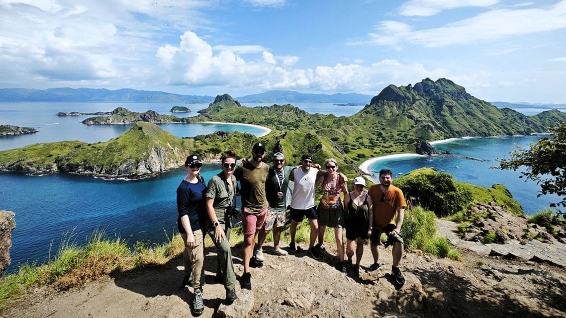 Eine WeRoad-Gruppe posiert auf einem Hügel mit Blick auf eine Bucht mit üppig grünen Inseln und türkisfarbenem Wasser.