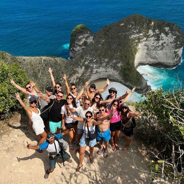 Eine WeRoad-Gruppenreise posiert für ein Foto auf einer Klippe mit Blick auf eine felsige Küste und ein türkisfarbenes Meer.