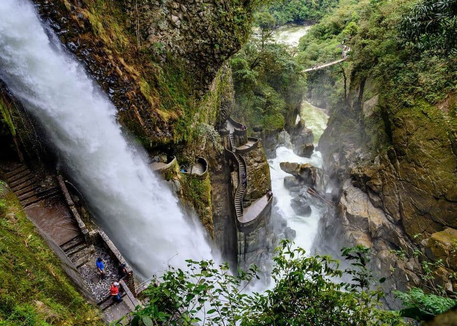 A group of people from a WeRoad trip on a steep, winding stone staircase beside a large waterfall in a rocky, green gorge.