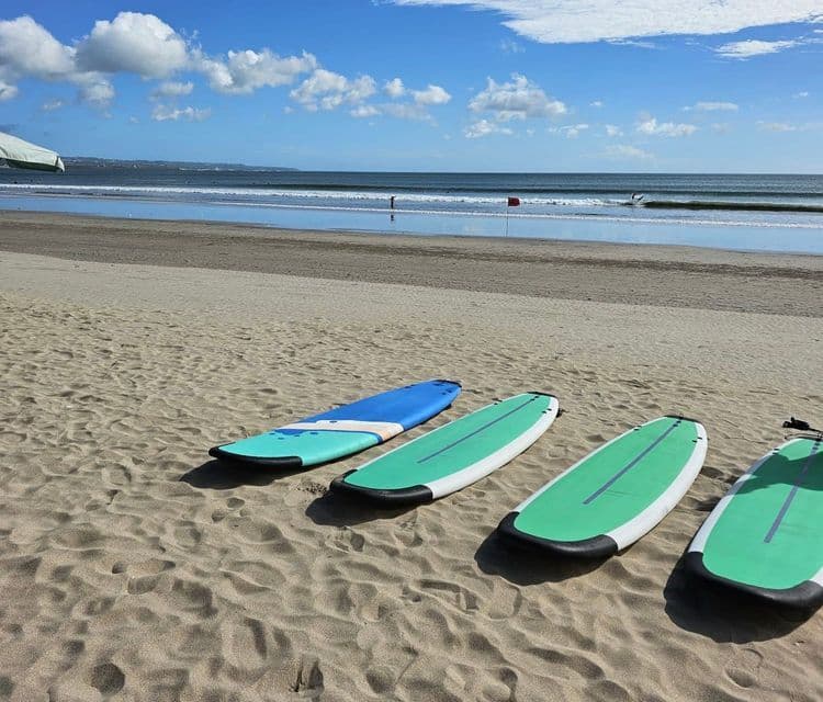 Vier Surfbretter liegen an einem Sandstrand mit dem Meer und einem teilweise bewölkten Himmel im Hintergrund.