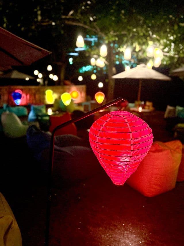 Eine rote Papierlaterne beleuchtet nachts eine Outdoor-Lounge, mit bunten Sitzsäcken und weiteren Laternen im Hintergrund.