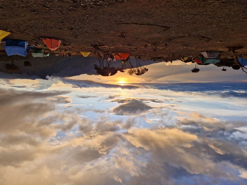 A WeRoad group trip campsite with colorful tents on a mountainside, seen above a sea of clouds during a golden sunset.