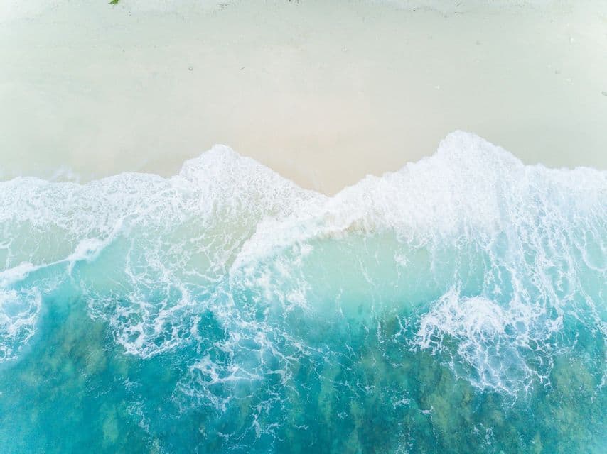 Vista aérea de olas turquesas con espuma blanca sobre una playa de arena.