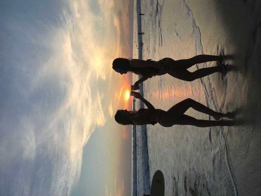 Due persone di un viaggio di gruppo WeRoad sono in silhouette su una spiaggia, che brindano al tramonto.