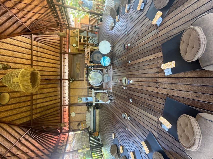 Uno studio di meditazione all'aperto con pavimenti in legno, tappetini, cuscini e gong disposti in cerchio per una sessione di gruppo.