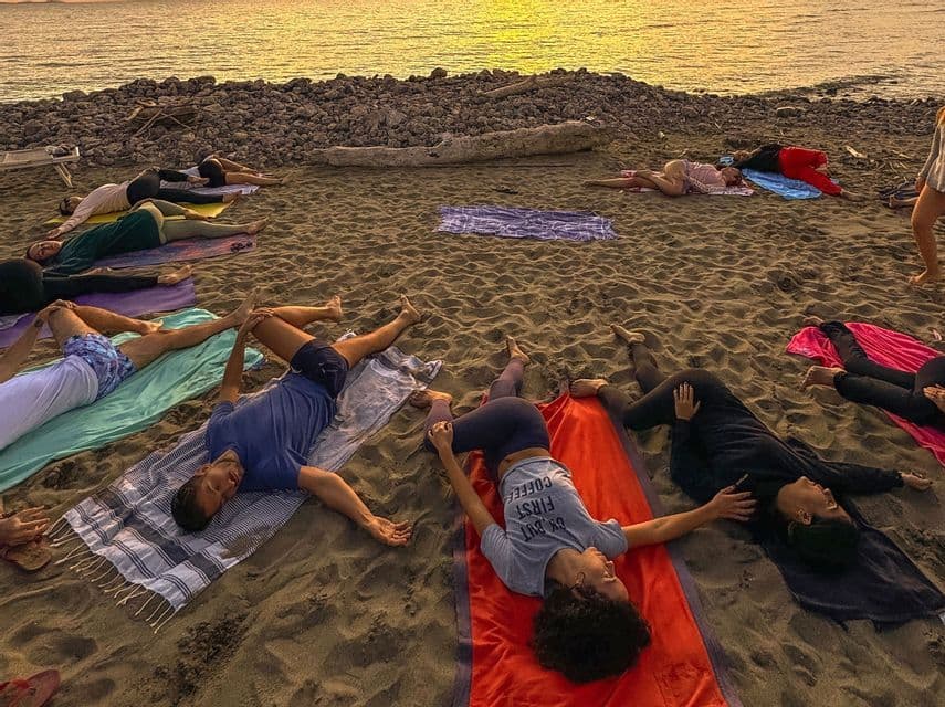 Un viaggio di gruppo WeRoad che pratica yoga su teli in una spiaggia sabbiosa al tramonto.