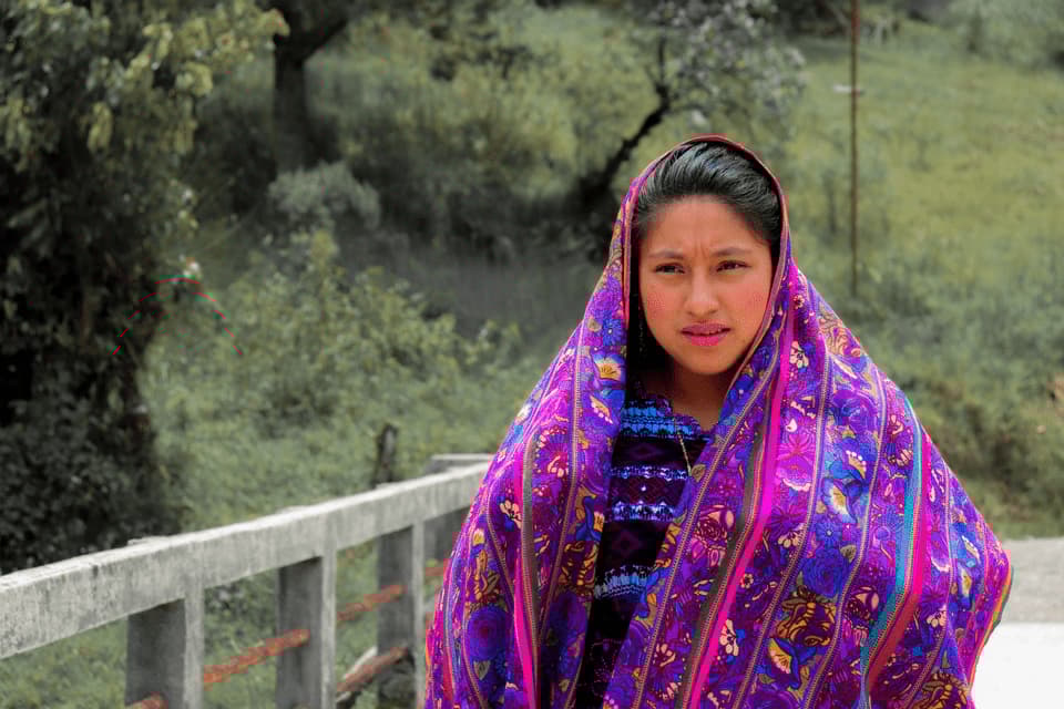 Eine junge Frau blickt in die Kamera, während sie einen leuchtenden, lila-blauen gemusterten Schal trägt, der ihren Kopf bedeckt.