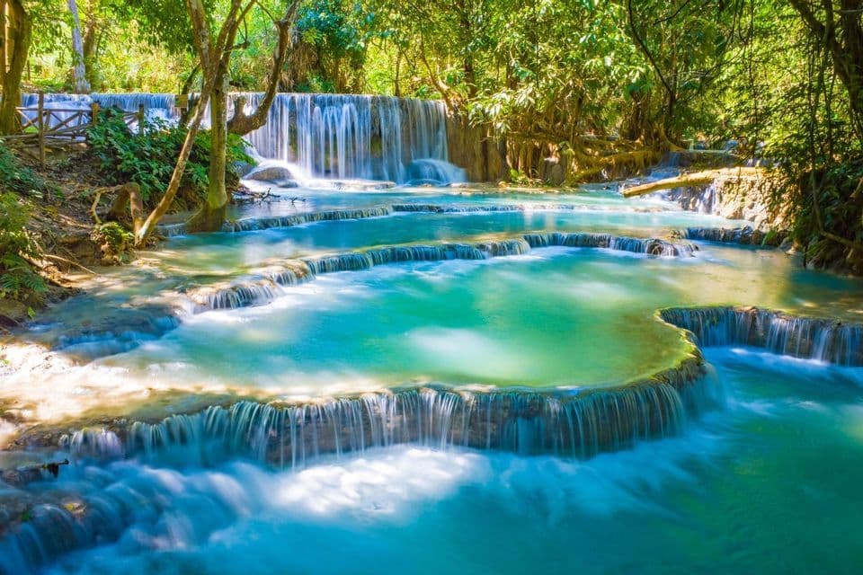 Ein mehrstufiger Wasserfall mit lebhaft türkisblauem Wasser, das über Kalksteinterrassen in einem üppig grünen Wald herabstürzt.