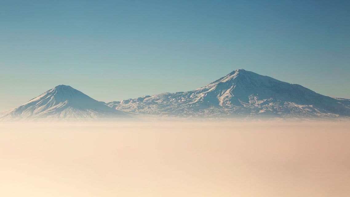 Due cime montuose innevate emergono da una spessa coltre di nuvole sotto un cielo azzurro e limpido.