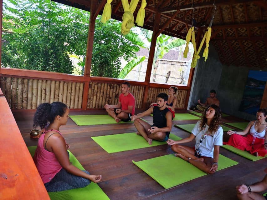 Eine WeRoad-Gruppe sitzt in Meditationshaltung auf grünen Yogamatten in einem hölzernen Freiluftpavillon.