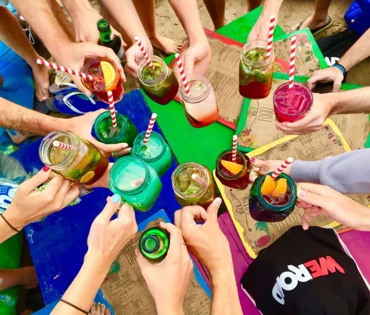 Blick von oben auf eine WeRoad Gruppe, die am Strand mit bunten Cocktails in Einmachgläsern anstößt.