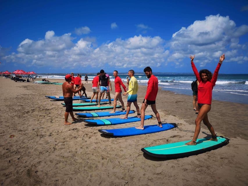 Un viaje en grupo de WeRoad con una clase de surf en una playa de arena, practicando cómo ponerse de pie en las tablas de surf con un instructor.