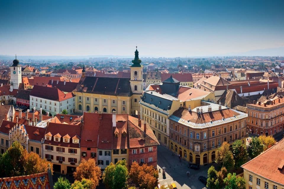 Vue aérienne d'une ville européenne avec des toits en terre cuite, des bâtiments historiques et un clocher sous un ciel dégagé.