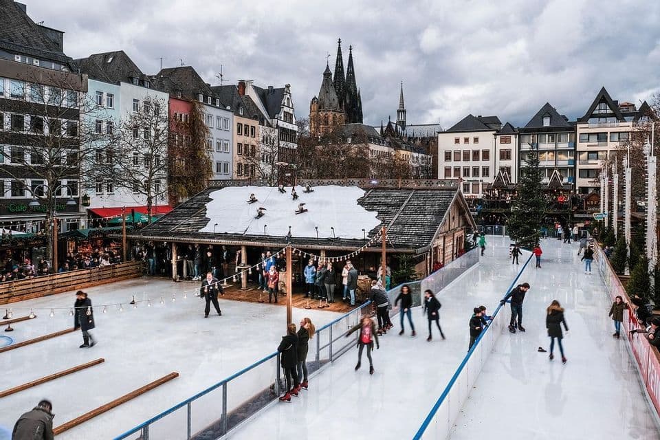 Persone che pattinano sul ghiaccio su una pista all'aperto in una piazza cittadina, con una cattedrale e edifici tradizionali sotto un cielo nuvoloso.