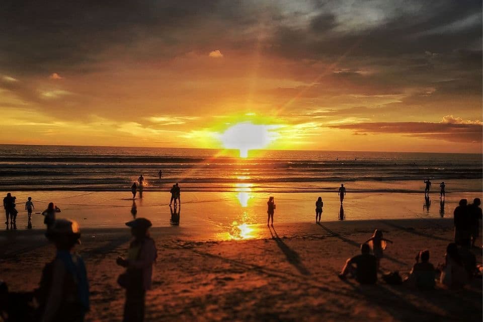Silhouetten einer WeRoad-Gruppenreise beobachten einen leuchtend orangefarbenen Sonnenuntergang über dem Meer von einem Sandstrand aus.