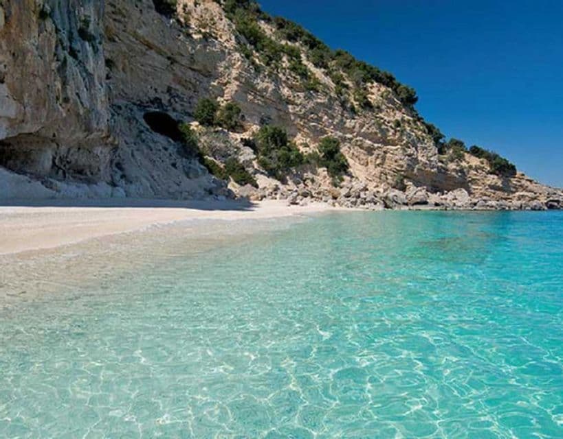 Acqua turchese limpida lambisce una spiaggia di sabbia bianca appartata, incastonata contro una grande scogliera rocciosa.