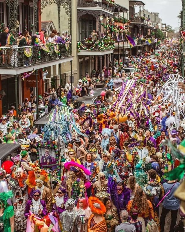 A high-angle view of a crowded street parade with participants wearing elaborate, colorful costumes and masks.