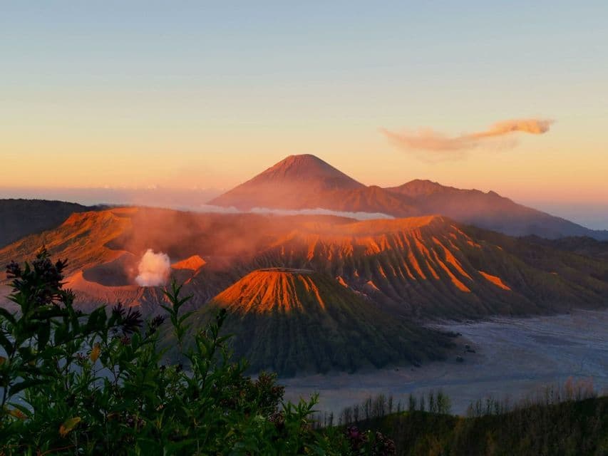 Una vista panorámica de cráteres volcánicos humeantes y montañas iluminadas por la cálida luz del amanecer.