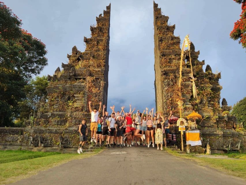 Un voyage en groupe WeRoad avec des gens qui sautent et sourient pour une photo devant une grande porte en pierre ornée, entourée d'arbres.