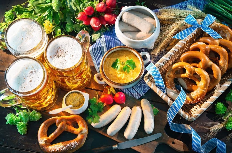 Una comida bávara tradicional con cerveza, pretzels y salchichas blancas está servida en una mesa de madera.