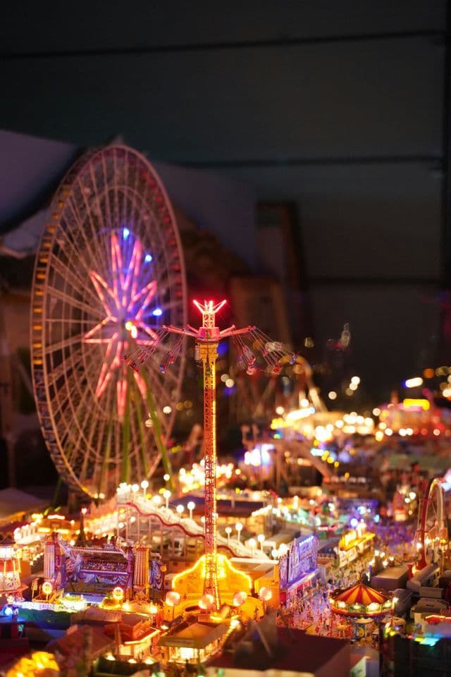 Una maqueta de parque de atracciones en miniatura, brillantemente iluminada con luces de colores por la noche, con una gran noria y un columpio.