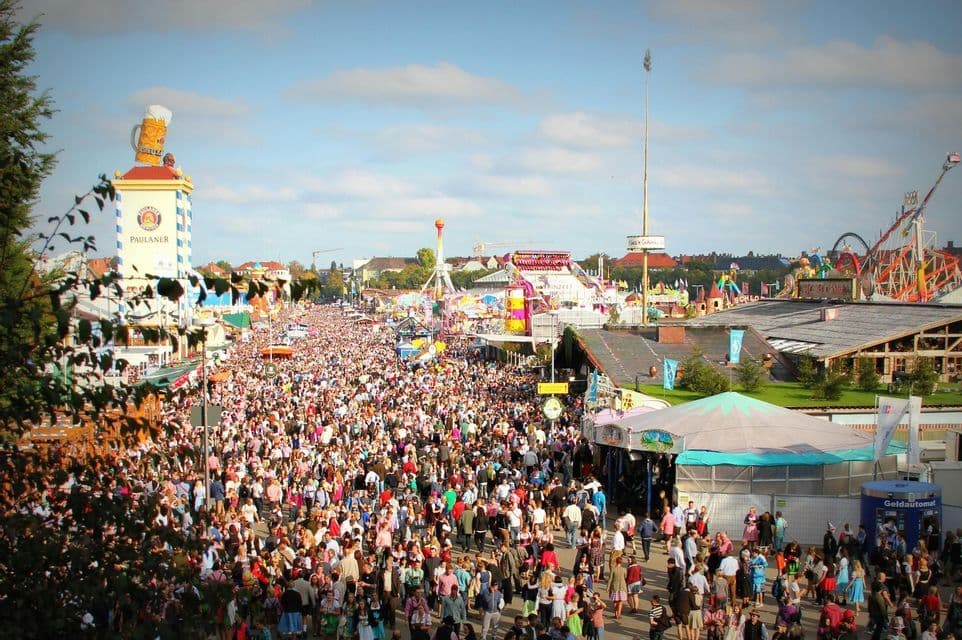 Una vista aérea de una multitud masiva de personas en un festival al aire libre, con tiendas de campaña, atracciones y una gran torre de cerveza.