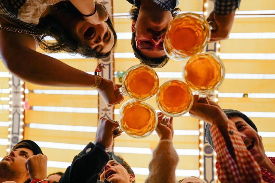 Una vista en ángulo bajo de un grupo de viaje de WeRoad brindando con jarras de cerveza de cristal contra un techo a rayas.