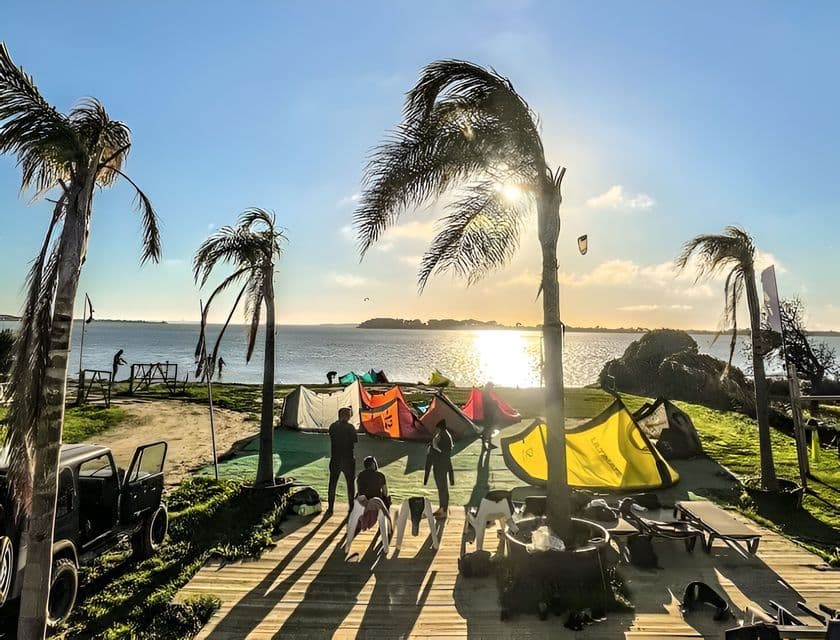 Un viaje en grupo de WeRoad prepara equipo de kitesurf en una cubierta de madera junto al agua, rodeado de palmeras al atardecer.