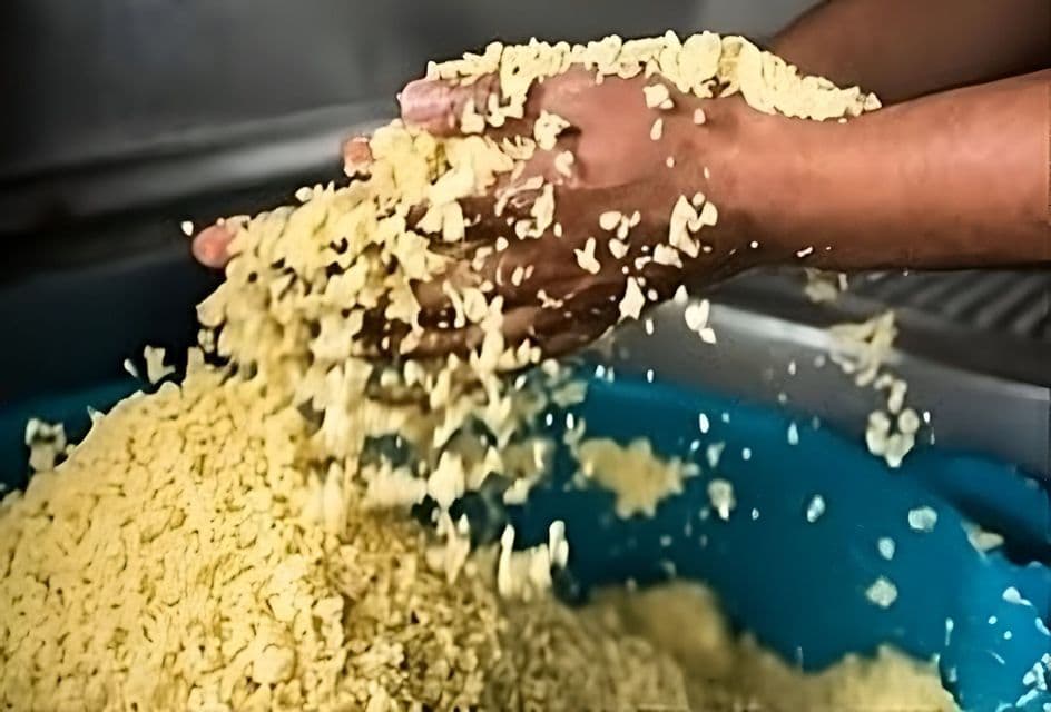 Primer plano de manos tamizando cuscús amarillo en un cuenco azul grande.