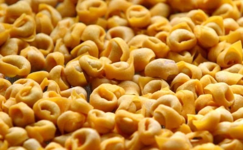 Un grande mucchio di tortellini freschi e crudi riempie l'inquadratura in un primo piano.