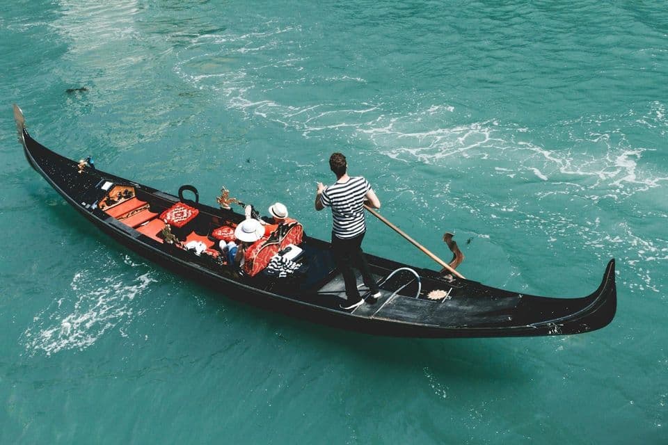 A gondolier rowing a WeRoad group trip in a black gondola on turquoise water.