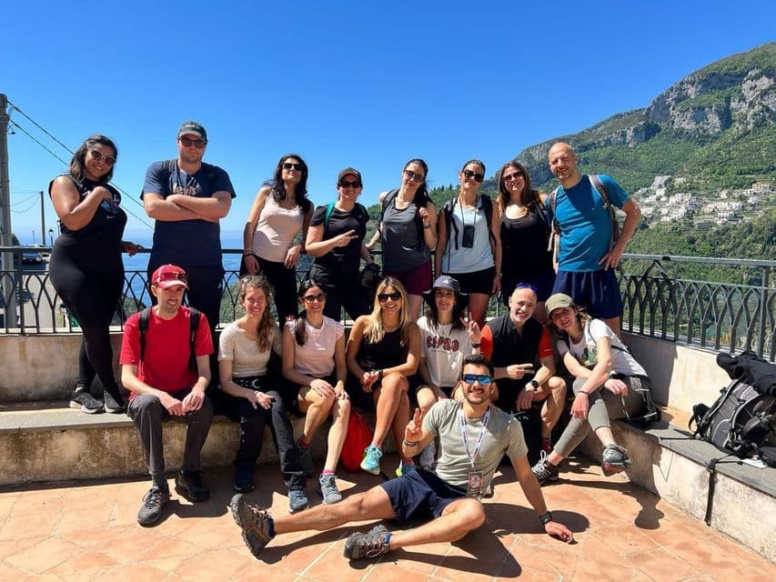 Un grupo de WeRoad posa para una foto en una terraza soleada con vistas a una costa montañosa y al mar.
