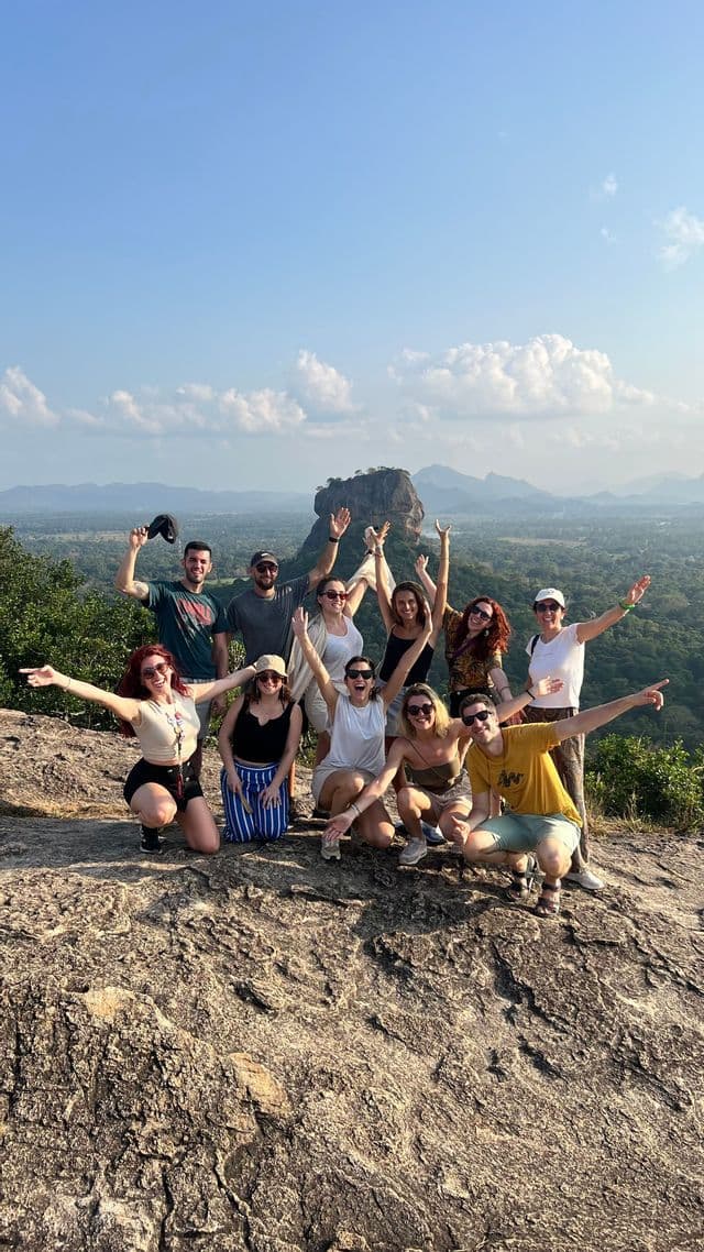 Un groupe WeRoad posant ensemble sur un point de vue rocheux, avec un vaste paysage verdoyant et des montagnes en arrière-plan.