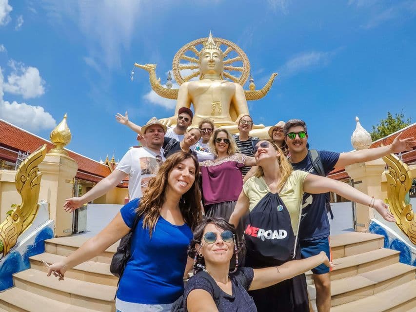 Un grupo de WeRoad posando para una selfie en las escaleras de un templo frente a una gigante estatua dorada de Buda.
