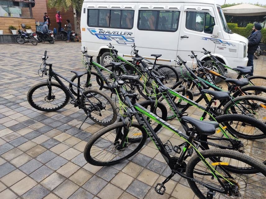 File di mountain bike nere e verdi sono parcheggiate su un cortile pavimentato davanti a un furgone turistico bianco.
