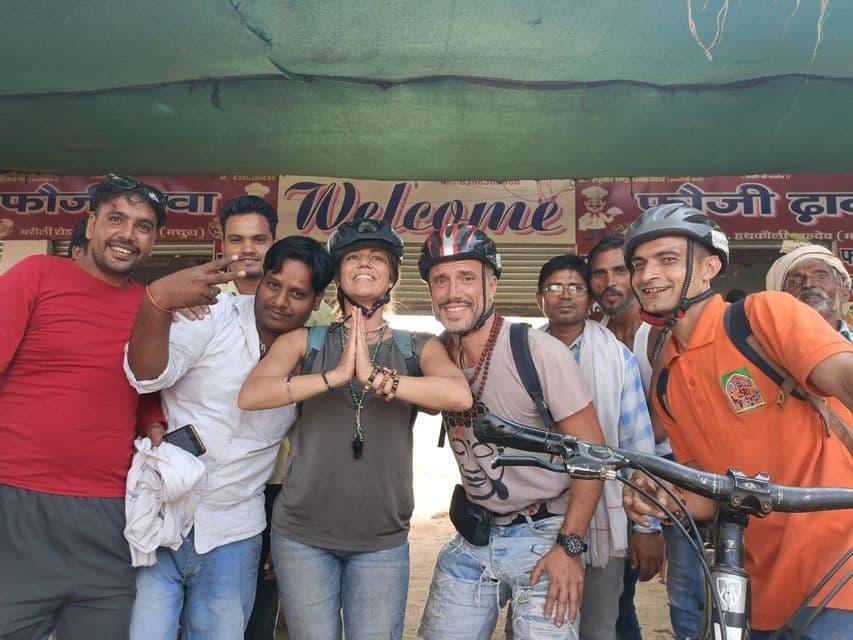 Un gruppo WeRoad sorridente in viaggio posa con uomini del posto; due viaggiatori indossano caschi da bici.