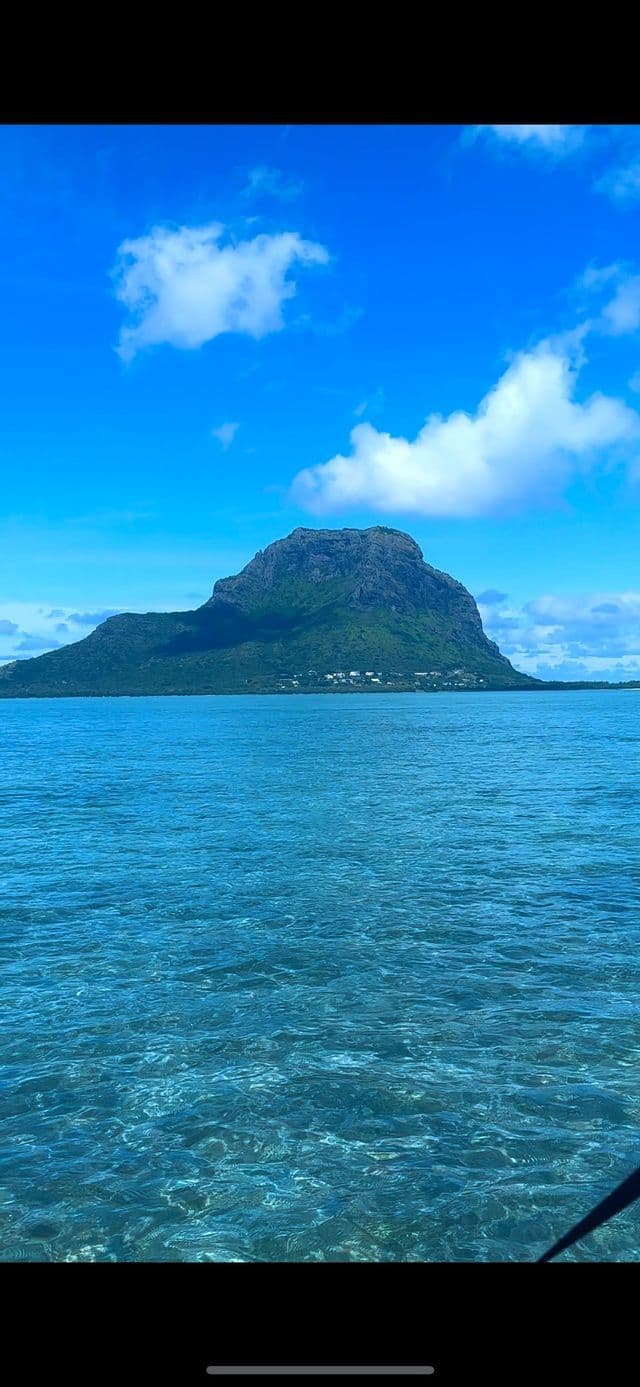 Una montaña verde y rocosa se eleva desde el mar turquesa bajo un cielo azul con nubes blancas.