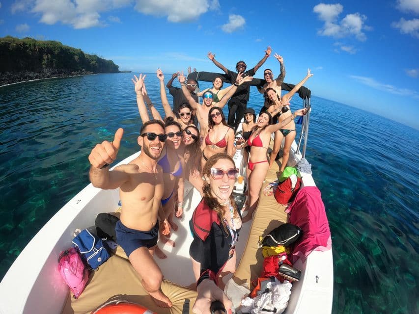 Un viaje en grupo de WeRoad posando para una selfie en un barco, flotando en aguas cristalinas de color turquesa cerca de una costa verde.
